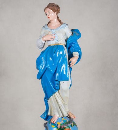 Zdjęcie nr 1: Podstawa feretronu w formie dwóch uproszczonych wolut z otworami na drążki, na płaskich podstawach. Na nich pełnoplastyczna figura Matki Boskiej w typie Niepokalanie Poczętej, stojąca na globie ziemskim, depcząca oplatającego go węża, który trzyma w paszczy jabłko. Maria ukazana w kontrapoście, z prawą nogą wysuniętą do przodu, lewą odwiedzioną, zgiętą w kolanie; prawą rękę składa na piersi, lewą, opuszczoną przytrzymuje płaszcz. Głowa przechylona w prawą stronę; twarz owalna z szeroko otworzonymi, niebieskimi oczami poniżej uniesionych brwi, z prostym nosem i drobnymi, ciemnoczerwonymi ustami, otoczona brązowymi, upiętymi w kok włosami, z wolnymi pasmami spływającymi na lewe ramię i plecy. Madonna ubrana w białą suknię z szerokim  jasnoniebieskim kołnierzem wiązanym na dekolcie, przepasaną złotym paskiem oraz błękitny płaszcz, który układając się w grube fałdy otacza jej lewą rękę, przechodzi przez prawe biodro i jest zatknięty z przodu za pasek.