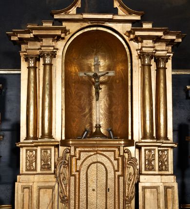 Zdjęcie nr 4: Ołtarz architektoniczny, jednoosiowy, dwukondygnacyjny, z bramkami, na cokole. Pierwsza kondygnacja ujęta parą pilastrów za dwiema parami gładkich kolumn o kapitelach kompozytowych, dźwigających imposty, z gzymsem wyłamanym w partii podpór. Środkowa para wysunięta przed lico ołtarza, zwieńczona trójkątnym przyczółkiem z rzeźbą przedstawiającą Boga Ojca w obłokach. Pole środkowe w formie arkady z obrazem Ukrzyżowania. Kondygnacja ujęta uszami utworzonymi z ornamentu małżowinowo-chrząstkowego. Na bramkach figury św. Piotra i św. Pawła. Druga kondygnacja w formie leżącego prostokąta, ujęta parą pilastrów i stojącą przed nimi parą gładkich kolumn o kapitelach kompozytowych, dźwigających imposty. Kondygnacja flankowana dwiema figurami aniołów stojących na postumentach. Pole obrazowe z przedstawieniem Chrystusa w Ogrójcu w formie leżącego owalu w prostokątnej płycinie. Zwieńczenie przyjmujące kształt impostu dźwigającego na szerokim gzymsie owalny kartusz ujęty ornamentem małżowinowo-chrząstkowym z przedstawieniem Veraicon. Nastawa pokryta bogatą dekoracją ornamentalną. W partii cokołów płyciny z ornamentem małżowinowo-chrząstkowym, w wewnętrznych dodatkowo główki anielskie oraz girlandy utworzone z tkaniny nad arkadami bramek. Czoło arkady pola środkowego dekorowane rozetami, w ościeżach bocznych małżowina, w podłuczu kasetony z rozetami. W przyłuczu arkady ornament roślinny. W impostach, w partii fryzu rozety, powyżej ażurowy ornament małżowinowo-chrząstkowy dekoruje podstawę gzymsu. Przyczółek ozdobiony małżowiną. W drugiej kondygnacji owalna rama obrazu przyjmuje postać wieńca laurowego dekorowanego kartuszami z kaboszonami. W narożach płyciny małżowina. Pole ujęte festonami utworzonymi z tkaniny, owoców i kwiatów. Fryz impostów dekorowany analogicznie jak w pierwszej kondygnacji. Na fragmentach belkowania wazony. Odcinki gzymsu połączone girlandą z tkaniny z pękiem owoców i kwiatów. Kondygnacja ujęta uszami z ornamentu małżowinowo-chrząstkowego. 
Ołtarz kamienny z drewnianą obudową i mensą z portatylem. Antepedium w formie leżącego prostokąta, ujęte ornamentalną ramą z motywem akantu. W polu purpurowa tkanina z haftowanym monogramem IHS. Nastawa polichromowana na kolor czarny ze złoconymi kolumnami, detalami architektonicznymi i ornamentyką.