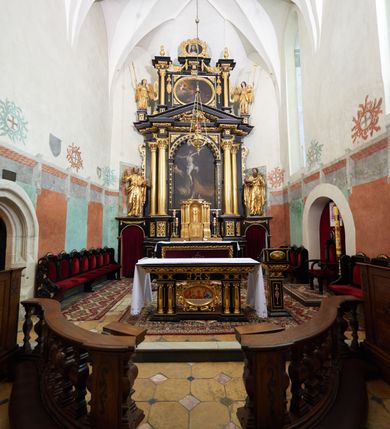Zdjęcie nr 5: Ołtarz architektoniczny, jednoosiowy, dwukondygnacyjny, z bramkami, na cokole. Pierwsza kondygnacja ujęta parą pilastrów za dwiema parami gładkich kolumn o kapitelach kompozytowych, dźwigających imposty, z gzymsem wyłamanym w partii podpór. Środkowa para wysunięta przed lico ołtarza, zwieńczona trójkątnym przyczółkiem z rzeźbą przedstawiającą Boga Ojca w obłokach. Pole środkowe w formie arkady z obrazem Ukrzyżowania. Kondygnacja ujęta uszami utworzonymi z ornamentu małżowinowo-chrząstkowego. Na bramkach figury św. Piotra i św. Pawła. Druga kondygnacja w formie leżącego prostokąta, ujęta parą pilastrów i stojącą przed nimi parą gładkich kolumn o kapitelach kompozytowych, dźwigających imposty. Kondygnacja flankowana dwiema figurami aniołów stojących na postumentach. Pole obrazowe z przedstawieniem Chrystusa w Ogrójcu w formie leżącego owalu w prostokątnej płycinie. Zwieńczenie przyjmujące kształt impostu dźwigającego na szerokim gzymsie owalny kartusz ujęty ornamentem małżowinowo-chrząstkowym z przedstawieniem Veraicon. Nastawa pokryta bogatą dekoracją ornamentalną. W partii cokołów płyciny z ornamentem małżowinowo-chrząstkowym, w wewnętrznych dodatkowo główki anielskie oraz girlandy utworzone z tkaniny nad arkadami bramek. Czoło arkady pola środkowego dekorowane rozetami, w ościeżach bocznych małżowina, w podłuczu kasetony z rozetami. W przyłuczu arkady ornament roślinny. W impostach, w partii fryzu rozety, powyżej ażurowy ornament małżowinowo-chrząstkowy dekoruje podstawę gzymsu. Przyczółek ozdobiony małżowiną. W drugiej kondygnacji owalna rama obrazu przyjmuje postać wieńca laurowego dekorowanego kartuszami z kaboszonami. W narożach płyciny małżowina. Pole ujęte festonami utworzonymi z tkaniny, owoców i kwiatów. Fryz impostów dekorowany analogicznie jak w pierwszej kondygnacji. Na fragmentach belkowania wazony. Odcinki gzymsu połączone girlandą z tkaniny z pękiem owoców i kwiatów. Kondygnacja ujęta uszami z ornamentu małżowinowo-chrząstkowego. 
Ołtarz kamienny z drewnianą obudową i mensą z portatylem. Antepedium w formie leżącego prostokąta, ujęte ornamentalną ramą z motywem akantu. W polu purpurowa tkanina z haftowanym monogramem IHS. Nastawa polichromowana na kolor czarny ze złoconymi kolumnami, detalami architektonicznymi i ornamentyką.