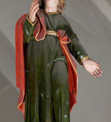 Zdjęcie nr 6: Trójfigurowa grupa Ukrzyżowania, rzeźby pełne. W środku znajduje się krucyfiks z postacią umarłego Chrystusa przybitego trzema gwoździami do krzyża. Chrystus w lekkim zwisie, o szeroko rozłożonych ramionach, bezwładny, głowa opuszczona na prawe ramię. Twarz szczupła, owalna, o prostym nosie, dużych oczach i na wpół otwartych ustach, okolona długim zarostem. Włosy w postaci delikatnych fal opadają na plecy i prawe ramię. Na głowie korona cierniowa. Ciało wychudzone o wyraźnie zarysowanej anatomii. Perizonium w formie tkaniny przewiązanej podwójnym sznurem, odsłaniającej prawe biodro, z dłuższym brzegiem zwisającym po prawej stronie. Draperia gęsto fałdowana, sztywna, o twardych załamaniach materiału. Na szczycie pionowej belki titulus w formie banderoli z napisem „INRI”. Figura Matki Boskiej ustawiona po lewej stronie, zwrócona lekko w stronę krzyża, z głową uniesioną w kierunku Chrystusa. Lewa ręka przyciśnięta do piersi przytrzymuje płaszcz, prawa opuszczona jest wzdłuż ciała. Twarz owalna, niemal bez cech indywidualnych. Ubrana w długą czerwoną suknię, błękitny płaszcz z szarym podbiciem i złoconymi lamówkami, przewiązany diagonalnie przez lewe ramię, opadający na plecy, podtrzymywany na piersi. Na głowie biały welon, opadający na ramiona i plecy. Figura św. Jana Ewangelisty po prawej stronie. Zwrócony delikatnie w stronę krzyża, w kontrapoście, z głową uniesioną w kierunku Chrystusa. Ręce rozpostarte, prawa ugięta i uniesiona w górę, lewa odwiedziona od boku. Twarz młoda, owalna o słabo zindywidualizowanych rysach, włosy w postaci loków sięgają ramion. Święty jest ubrany w ciemnozieloną tunikę przepasaną w talii sznurem oraz czerwony płaszcz ze złoconymi lamówkami, przerzucony diagonalnie przez prawe przedramię i plecy. Matka Boska i św. Jan wykonują podobne gesty; draperie okrywających ich szat są sztywne, ostro załamane. Między figurami Chrystusa i towarzyszącymi mu osobami występuje hierarchia wielkości.