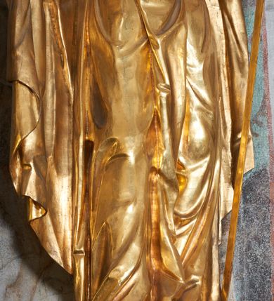 Zdjęcie nr 3: Rzeźba pełna, na niewysokim postumencie, przestawiająca stojącego św. Pawła wyobrażonego w całej postaci. Święty zwrócony frontalnie do widza, z głową skierowaną w prawo, w lekkim kontrapoście; prawa stopa wysunięta do przodu wystaje spod połów szaty. Obie ręce ugięte, wysunięte w przód; w prawej dłoni księga, w lewej miecz skierowany ostrzem w dół. Twarz podłużna, szczupła, z długim, ostrym nosem oraz delikatnie zarysowanymi oczami i ustami, okolona długą brodą, spływającą w postaci pukli na piersi. Włosy krótkie, gęste, kręcone. Święty jest ubrany w tunikę przepasaną w talii sznurem oraz płaszcz przewieszony diagonalnie przez lewe ramię i opadający na plecy. Draperia ekspresyjnie marszczona i fałdowana w partii tuniki, płaszcz w postaci ciężkiej tkaniny obficie drapowanej w grube fałdy opada swobodnie w dół. W partiach ciała polichromia naturalistyczna, szaty złocone, atrybuty polichromowane i delikatnie złocone.