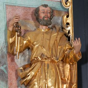 Zdjęcie nr 1: Rzeźba pełna, na niewysokim postumencie, przestawiająca św. Piotra. Święty zwrócony frontalnie do widza, z głową skręconą nieznacznie w lewo, ukazany w lekkim kontrapoście; lewa stopa wysunięta do przodu wystaje spod szaty. Obie ręce zgięte, uniesione, w prawej dłoni dwa klucze, lewa zwrócona ku górze. Twarz pociągła, szczupła, z dużym, ostrym nosem oraz delikatnie zarysowanymi ustami i oczami. Okolona stosunkowo krótką, falowaną brodą; włosy krótkie w formie pukli. Święty jest ubrany w długą tunikę, zapinaną pod szyją na guziki, przepasaną sznurem w talii oraz płaszcz przewieszony przez lewe ramię, opadający przez plecy, zawinięty wokół prawego biodra i zatknięty z przodu za pasek. Draperia ukształtowana miękko, o delikatnych fałdowaniach tuniki oraz grubych załamaniach ciężkiej tkaniny płaszcza. Polichromia w partiach ciała naturalistyczna, szaty i atrybuty złocone.