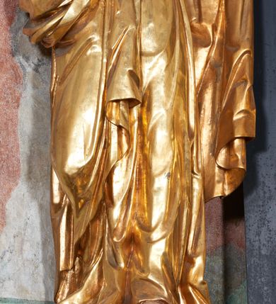 Zdjęcie nr 4: Rzeźba pełna, na niewysokim postumencie, przestawiająca św. Piotra. Święty zwrócony frontalnie do widza, z głową skręconą nieznacznie w lewo, ukazany w lekkim kontrapoście; lewa stopa wysunięta do przodu wystaje spod szaty. Obie ręce zgięte, uniesione, w prawej dłoni dwa klucze, lewa zwrócona ku górze. Twarz pociągła, szczupła, z dużym, ostrym nosem oraz delikatnie zarysowanymi ustami i oczami. Okolona stosunkowo krótką, falowaną brodą; włosy krótkie w formie pukli. Święty jest ubrany w długą tunikę, zapinaną pod szyją na guziki, przepasaną sznurem w talii oraz płaszcz przewieszony przez lewe ramię, opadający przez plecy, zawinięty wokół prawego biodra i zatknięty z przodu za pasek. Draperia ukształtowana miękko, o delikatnych fałdowaniach tuniki oraz grubych załamaniach ciężkiej tkaniny płaszcza. Polichromia w partiach ciała naturalistyczna, szaty i atrybuty złocone.