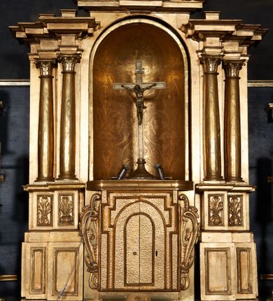 Zdjęcie nr 1: Główna część tabernakulum w formie zbliżonej do sześcianu z drzwiczkami dekorowanymi motywem podwójnej bramy i krzyża, uformowanym z listewek; drzwiczki ujęte po bokach uszami z ornamentu małżowinowo-chrząstkowego. Nad tą sześcienną częścią tron wystawienia z obudową architektoniczną w formie aediculi, w centrum której nisza półkolista zamknięta sferycznie z wstawionym krzyżem ołtarzowym. Nisza ujęta dwiema parami pilastrów i kolumn o kapitelach korynckich, ustawionych na podwójnych cokołach, w dwóch strefach; cokoły rozmieszczone są u dołu tabernakulum i po bokach jego sześciennej części głównej. Podpory dźwigają pełne belkowanie wyłamane na ich osi. Całość zwieńczona przerwanym przyczółkiem o wklęsłych bokach. Górne cokoły dekorowane są płycinami z liśćmi akantu. Nisza z rytą dekoracją w postaci czterolistnych pól z dekoracją roślinną, liliami heraldycznymi i krzyżami, z otwartą koroną w centrum kompozycji. 
