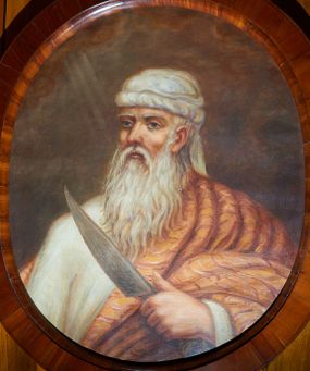 Zdjęcie nr 1: Obraz w kształcie owalu z przedstawieniem Abrahama ukazanego w popiersiu, zwróconego w prawą stronę z nożem w lewej dłoni. Twarz pociągła o rysach starca, okolona siwymi włosami i długą, siwą brodą. Abraham ubrany jest w białą suknię z długimi rękawami, jasnobrązowy płaszcz zdobiony w czerwone paski oraz biały turban na głowie. Tło jednolite brązowe, po lewej stronie niewielkie obłoki z promieniami. Rama drewniana, fornirowana, politurowana.