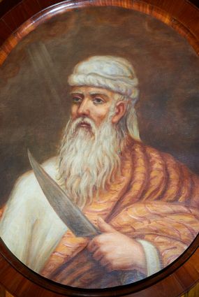 Zdjęcie nr 1: Obraz w kształcie owalu z przedstawieniem Abrahama ukazanego w popiersiu, zwróconego w prawą stronę z nożem w lewej dłoni. Twarz pociągła o rysach starca, okolona siwymi włosami i długą, siwą brodą. Abraham ubrany jest w białą suknię z długimi rękawami, jasnobrązowy płaszcz zdobiony w czerwone paski oraz biały turban na głowie. Tło jednolite brązowe, po lewej stronie niewielkie obłoki z promieniami. Rama drewniana, fornirowana, politurowana.