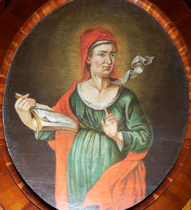 Zdjęcie nr 1: Obraz w kształcie stojącego owalu, przedstawiający św. Annę. Święta ukazana w centrum kompozycji, do wysokości kolan, z głową skierowaną w lewą stronę. W prawej dłoni trzyma otwartą księgę, a lewą rękę unosi z wyprostowanym palcem wskazującym, czyniąc gest nauczania. Twarz o długim, prostym nosie, wąskich ustach z silnie podkreśloną linią szyi. Oczy migdałowe, niebieskie, nad nimi proste ciemne brwi. Święta ubrana jest w z zieloną suknię, przewiązaną pod biustem, białą chustę oraz czerwony płaszcz założony na głowę. Tło ciemnobrązowe, rozświetlone wokół głowy świętej. Rama drewniana, fornirowana, politurowana.