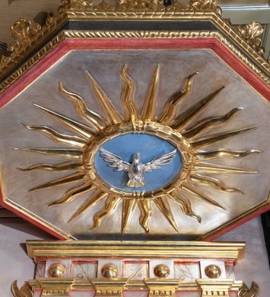 Zdjęcie nr 6: Ambona przyścienna, ustawiona na rzeźbionym konarze, rozwarstwiającym się na pnącza ujmujące kosz. Kosz na planie ośmioboku na cokoliku, u spodu podwieszona półkula. Ścianki wydzielone rzeźbionymi pnączami z winnym gronem. W polach płytkie nisze, wsparte na cokolikach, wypełnione okuciami przechodzącymi w wić roślinną, u góry zamknięte półkoliście z konchami. Ścianki w dwóch trzecich wysokości włącznie z wnękami obiega profilowany gzyms. Parapet kosza w formie gzymsu dekorowany głębokim kimationem. Zaplecek o kształcie stojącego prostokąta wypełnionego kanelurami, zamkniętego fryzem z metopami zdobionymi kulami; ujęty strzępionymi liśćmi palmowymi. Baldachim na planie analogicznym względem kosza, płaski, zwieńczony palmetami; na podniebiu rzeźbiona gołębica Ducha Świętego w medalionie utworzonym z liśćmi wawrzynu, w glorii promienistej. Struktura polichromowana na kolor czarny, podwieszenie kosza na kolor biały; ornamentyka, profilowania i detale złocone, srebrzone oraz polichromowane na czerwono. Ornamentyka na koszu dodatkowo pokryta laserunkiem. 