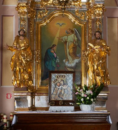 Zdjęcie nr 6: Rzeźba drążona, ustawiona na prostopadłościennym cokole. Figura ukazana frontalnie, w silnym kontrapoście z prawą nogą ugiętą w kolanie, z głową skierowaną w lewo, z dwoma rękami wyciągniętymi w prawą stronę. Twarz szczupła, pociągła, wyraźnie zarysowane linie łuków brwiowych, nosa i kości policzkowych; oczy niewielkie, głęboko osadzone, nos wąski, prosty, usta pełne, rozchylone; okolona krótką, kręconą brodą. Włosy krótkie, głęboko rzeźbione w pojedyncze pukle, opadające na plecy. Święty ubrany jest w suknię rozchyloną na piersi, z kołnierzykiem; przepasaną szarfą w talii; rękawy długie z podwiniętym brzegiem; tkanina ściśle przylegająca do ciała, marszczona, silnie drapowana. Płaszcz przerzucony przez lewe ramię, otaczający postać i zawinięty na prawym boku, z fragmentem upiętym u pasa; tkanina silnie drapowana, o wywiniętym brzegu i rozwianych fragmentach. Polichromia naturalistyczna w odsłoniętych partiach ciała, szata złocona.
