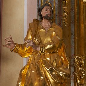 Zdjęcie nr 1: Rzeźba drążona, ustawiona na prostopadłościennym cokole. Figura ukazana frontalnie, w silnym kontrapoście z prawą nogą ugiętą w kolanie, z głową skierowaną w lewo, z dwoma rękami wyciągniętymi w prawą stronę. Twarz szczupła, pociągła, wyraźnie zarysowane linie łuków brwiowych, nosa i kości policzkowych; oczy niewielkie, głęboko osadzone, nos wąski, prosty, usta pełne, rozchylone; okolona krótką, kręconą brodą. Włosy krótkie, głęboko rzeźbione w pojedyncze pukle, opadające na plecy. Święty ubrany jest w suknię rozchyloną na piersi, z kołnierzykiem; przepasaną szarfą w talii; rękawy długie z podwiniętym brzegiem; tkanina ściśle przylegająca do ciała, marszczona, silnie drapowana. Płaszcz przerzucony przez lewe ramię, otaczający postać i zawinięty na prawym boku, z fragmentem upiętym u pasa; tkanina silnie drapowana, o wywiniętym brzegu i rozwianych fragmentach. Polichromia naturalistyczna w odsłoniętych partiach ciała, szata złocona.