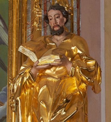 Zdjęcie nr 1: Rzeźba drążona, ustawiona na cokole. Figura ukazana frontalnie, w kontrapoście, obiema rękami podtrzymuje przed piersią otwartą księgę. Twarz pociągła, o wydłużonej szczęce; oczy duże, spoglądające w dół, nos prosty i duży, usta pełne; okolona krótką, kręconą brodą. Włosy krótkie, falowane. Święty ubrany jest w długą suknię z kołnierzykiem, z długimi rękawami o podwiniętym brzegu, przepasaną w talii szarfą; tkanina ściśle przylega do ciała, w partii torsu marszczona, delikatnie drapowana w zygzakowate fałdki w dolnej części. Płaszcz podtrzymywany na przedramionach, z obfitą partią materiału zawijającą się na lewej nodze; tkanina delikatnie rozwiana, miejscami zawinięta, silnie drapowana. Polichromia naturalistyczna w odsłoniętych partiach ciała, szaty i atrybuty złocone.