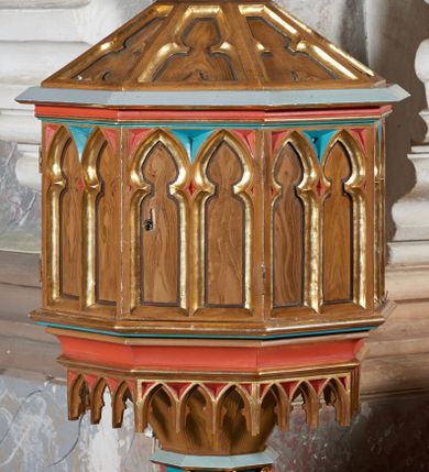 Zdjęcie nr 1: Stopa chrzcielnicy w formie ośmiobocznego, profilowanego cokołu. Trzon ośmioboczny, zwieńczony pierścieniem dekorowanym złoconymi rozetami. Czara ośmioboczna, ścianki zdobione parami blend, z ażurowymi arkadkami u spodu. Pokrywa na planie ośmioboku, zwężająca się ku górze, ze ściankami dekorowanymi płycinami w formie trójliścia,  zwieńczona cokołem z rzeźbioną sceną Chrztu Chrystusa. Po lewej stronie Chrystus w kontrapoście, z wykrokiem na prawą nogę, z rękami zbliżonymi do siebie (brak dłoni), pochyla nieznacznie głowę. Jest owinięty w czerwony, obszerny płaszcz z zielonym podbiciem i złotą lamówką, który przykrywa jego biodra i nogi. Ma pociągłą twarz, o małych oczach, wąskim nosie i ustach, wąsy, brodę, która dzieli się w dwa pukle i falowane włosy opadające na kark. Nie widać mu stóp, które są zanurzone w wodzie. Z jego lewej strony na fragmencie podłoża stoi św. Jan Chrzciciel, który opiera lewą rękę na kiju a prawą unosi ponad głową Chrystusa muszlę. Ma owalną twarz o podobnym do Chrystusa wyrazie i wywijające się włosy opadające na kark. Jest ubrany w tunikę z futra, a na nią ma zarzucony szary płaszcz z pomarańczowym podbiciem. 
Struktura w odcieniu ciemnego drewna, profile szare, niebieskie i czerwone, inne profile i ornamenty złocone.
