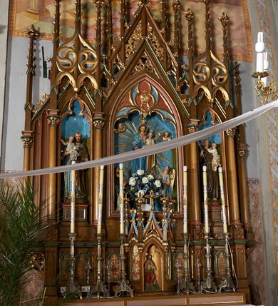Zdjęcie nr 2: Nastawa przyścienna, architektoniczna, trójosiowa, z architektonicznymi uszakami zakończonymi pinaklem, ustawiona na dwustopniowej podstawie. Mensa prostopadłościenna, skrzyniowa, drewniana z kamiennym portatylem. Antepedium ujęte w narożach ćwierćkolumienkami; pole dekorowane trzema płycinami, z których środkowa z motywem czworoliścia, boczne z parami blend. Retabulum ustawione na wysokim cokole, z predellą ozdobioną blendami. W partii środkowej predelli quasi tabernakulum na planie trzech boków  sześcioboku. Pośrodku nisza z figurą Najświętszego Serca Jezusa, ściany boczne w formie ostrołukowych płycin z płaskorzeźbioną dekoracją o motywie winnego grona i kłosów, wszystkie zwieńczone wimpergami flankowanymi pinaklami z kwiatonami. Nastawa w formie trzech ostrołukowych nisz dekorowanych maswerkiem, ujętych kolumienkami zakończonymi kapitelami utworzonymi ze stylizowanych rozet. Nisza środkowa szersza i wyższa, zakończona wimpergą wypełnioną koronę. Całość nastawy wieńczą strzeliste pinakle, połączone ze sobą motywem ażurowego maswerku, zwieńczone kwiatonami, dekorowane żabkami. W środkowej niszy figura Matki Boskiej z Dzieciątkiem. W kwaterach bocznych ustawione na cokołach figury św. Józefa po lewej i św. Antoniego Padewskiego po prawej stronie. Ołtarz utrzymany w kolorystyce ciemnego drewna z malowanymi niszami w kolorach niebieskim i czerwonym. Profile, detale i ornamenty zielone, czerwone lub złocone. 

