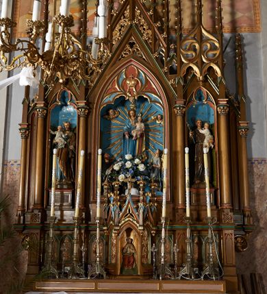 Zdjęcie nr 1: Nastawa przyścienna, architektoniczna, trójosiowa, z architektonicznymi uszakami zakończonymi pinaklem, ustawiona na dwustopniowej podstawie. Mensa prostopadłościenna, skrzyniowa, drewniana z kamiennym portatylem. Antepedium ujęte w narożach ćwierćkolumienkami; pole dekorowane trzema płycinami, z których środkowa z motywem czworoliścia, boczne z parami blend. Retabulum ustawione na wysokim cokole, z predellą ozdobioną blendami. W partii środkowej predelli quasi tabernakulum na planie trzech boków  sześcioboku. Pośrodku nisza z figurą Najświętszego Serca Jezusa, ściany boczne w formie ostrołukowych płycin z płaskorzeźbioną dekoracją o motywie winnego grona i kłosów, wszystkie zwieńczone wimpergami flankowanymi pinaklami z kwiatonami. Nastawa w formie trzech ostrołukowych nisz dekorowanych maswerkiem, ujętych kolumienkami zakończonymi kapitelami utworzonymi ze stylizowanych rozet. Nisza środkowa szersza i wyższa, zakończona wimpergą wypełnioną koronę. Całość nastawy wieńczą strzeliste pinakle, połączone ze sobą motywem ażurowego maswerku, zwieńczone kwiatonami, dekorowane żabkami. W środkowej niszy figura Matki Boskiej z Dzieciątkiem. W kwaterach bocznych ustawione na cokołach figury św. Józefa po lewej i św. Antoniego Padewskiego po prawej stronie. Ołtarz utrzymany w kolorystyce ciemnego drewna z malowanymi niszami w kolorach niebieskim i czerwonym. Profile, detale i ornamenty zielone, czerwone lub złocone. 

