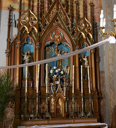 Zdjęcie nr 3: Nastawa przyścienna, architektoniczna, trójosiowa, z architektonicznymi uszakami zakończonymi pinaklem, ustawiona na dwustopniowej podstawie. Mensa prostopadłościenna, skrzyniowa, drewniana z kamiennym portatylem. Antepedium ujęte w narożach ćwierćkolumienkami; pole dekorowane trzema płycinami, z których środkowa z motywem czworoliścia, boczne z parami blend. Retabulum ustawione na wysokim cokole, z predellą ozdobioną blendami. W partii środkowej predelli quasi tabernakulum na planie trzech boków  sześcioboku. Pośrodku nisza z figurą Najświętszego Serca Jezusa, ściany boczne w formie ostrołukowych płycin z płaskorzeźbioną dekoracją o motywie winnego grona i kłosów, wszystkie zwieńczone wimpergami flankowanymi pinaklami z kwiatonami. Nastawa w formie trzech ostrołukowych nisz dekorowanych maswerkiem, ujętych kolumienkami zakończonymi kapitelami utworzonymi ze stylizowanych rozet. Nisza środkowa szersza i wyższa, zakończona wimpergą wypełnioną koronę. Całość nastawy wieńczą strzeliste pinakle, połączone ze sobą motywem ażurowego maswerku, zwieńczone kwiatonami, dekorowane żabkami. W środkowej niszy figura Matki Boskiej z Dzieciątkiem. W kwaterach bocznych ustawione na cokołach figury św. Józefa po lewej i św. Antoniego Padewskiego po prawej stronie. Ołtarz utrzymany w kolorystyce ciemnego drewna z malowanymi niszami w kolorach niebieskim i czerwonym. Profile, detale i ornamenty zielone, czerwone lub złocone. 

