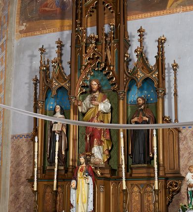 Zdjęcie nr 3: Nastawa ołtarzowa architektoniczna, jednokondygnacyjna, trójosiowa, ze zwieńczeniem. Ołtarz drewniany, skrzyniowy, mensa drewniana. Antepedium z narożami wypełnionymi ćwierćkolumienkami, dekorowane czterema blendami, z czworoliściem z gorejącym sercem pośrodku. Tabernakulum w formie prostopadłościennej szafki, ujęte w narożach kolumienkami dźwigającymi gzyms o kształcie łuku ostrego nadwieszonego dekorowanego żabkami i zwieńczonego pinaklem. Drzwiczki w formie stojącego prostokąta zamkniętego łukiem ostrym, zdobione płaskorzeźbionym motywem winnej latorośli, kłosów zbóż i monogramem IHS. Predella nastawy dekorowana blendami z malowaną dekoracją w formie winnego grona. 
Retabulum ołtarzowe w postaci trzech nisz zamkniętych łukami ostrymi, ujętych kolumienkami o kapitelach dekorowanych stylizowanymi rozetami i  dźwigającymi pinakle z żabkami i kwiatonami. Środkowa nisza zamknięta łukiem ostrym z krenelażem, ponad którym ażurowa konstrukcja utworzona z wimperg i pinakli, dekorowana żabkami i kwiatonami. Nisze boczne zwieńczone przeplatającymi się żebrami, dekorowanymi w polach rozetami i pinaklami zakończonymi kwiatonami. Zwieńczenie w formie ażurowej konstrukcji utworzonej z pinakli połączonych łukami przyporowymi, dekorowanymi krenelażem i żabkami, środkowy pinakiel najwyższy, zwieńczony krzyżem. W niszy środkowej figura Najświętsze Serce Jezusa, w bocznych: św. Teresa z Avila po lewej i św. Andrzej Bobola po prawej stronie. Nastawa ujęta uszami utworzonymi z przypór z pinaklami.
Ołtarz w kolorze ciemnego drewna, blendy i nisze polichromowane na niebiesko i zielono, profile, detale i ornamenty złocone.
