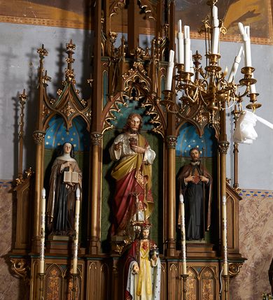 Zdjęcie nr 2: Nastawa ołtarzowa architektoniczna, jednokondygnacyjna, trójosiowa, ze zwieńczeniem. Ołtarz drewniany, skrzyniowy, mensa drewniana. Antepedium z narożami wypełnionymi ćwierćkolumienkami, dekorowane czterema blendami, z czworoliściem z gorejącym sercem pośrodku. Tabernakulum w formie prostopadłościennej szafki, ujęte w narożach kolumienkami dźwigającymi gzyms o kształcie łuku ostrego nadwieszonego dekorowanego żabkami i zwieńczonego pinaklem. Drzwiczki w formie stojącego prostokąta zamkniętego łukiem ostrym, zdobione płaskorzeźbionym motywem winnej latorośli, kłosów zbóż i monogramem IHS. Predella nastawy dekorowana blendami z malowaną dekoracją w formie winnego grona. 
Retabulum ołtarzowe w postaci trzech nisz zamkniętych łukami ostrymi, ujętych kolumienkami o kapitelach dekorowanych stylizowanymi rozetami i  dźwigającymi pinakle z żabkami i kwiatonami. Środkowa nisza zamknięta łukiem ostrym z krenelażem, ponad którym ażurowa konstrukcja utworzona z wimperg i pinakli, dekorowana żabkami i kwiatonami. Nisze boczne zwieńczone przeplatającymi się żebrami, dekorowanymi w polach rozetami i pinaklami zakończonymi kwiatonami. Zwieńczenie w formie ażurowej konstrukcji utworzonej z pinakli połączonych łukami przyporowymi, dekorowanymi krenelażem i żabkami, środkowy pinakiel najwyższy, zwieńczony krzyżem. W niszy środkowej figura Najświętsze Serce Jezusa, w bocznych: św. Teresa z Avila po lewej i św. Andrzej Bobola po prawej stronie. Nastawa ujęta uszami utworzonymi z przypór z pinaklami.
Ołtarz w kolorze ciemnego drewna, blendy i nisze polichromowane na niebiesko i zielono, profile, detale i ornamenty złocone.
