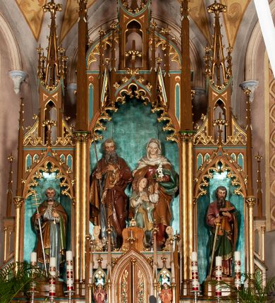 Zdjęcie nr 1: Nastawa ołtarzowa architektoniczna, jednokondygnacyjna, trójosiowa, ze zwieńczeniem. Ołtarz drewniany, skrzyniowy, mensa drewniana z marmurowym portatylem. Antepedium dekorowane czterem blendami, z czworoliściem z monogramem IHS w centrum. Tabernakulum w formie prostopadłościanu, dwukondygnacyjne, ze zwieńczeniem, na szerokiej podstawie. W dolnej kondygnacji dwoje drzwi dekorowanych ostrołukowymi blendami i przedzielonych służką. Wyżej tron wystawienia trójosiowy, w postaci trzech nisz zamkniętych łukiem ostrym, ujętych służkami dźwigającymi pinakle. Oś środkowa wyższa, z dwuskrzydłowymi drzwiczkami przedzielonymi służką i dekorowanymi płaskorzeźbioną winną latoroślą z kłosami zbóż. W niszach bocznych figury adorujących aniołów. Całość zwieńczona postumentem na relikwie. Retabulum ołtarzowe w postaci trzech nisz zamkniętych łukami ostrymi z ażurowym fryzem arkadkowym, dekorowanym po bokach blendami; osie wydzielone służkami, podwójnymi w osi środkowej, dźwigającymi pinakle z żabkami i kwiatonami. Osie zwieńczone ażurowymi wieżyczkami przeprutymi łukami trójlistnymi ostrymi, których pierwszą kondygnację kończy łuk odwrócony,  dekorowany pinaklami i żabkami, zwieńczony kwiatonem. Wieżyczki ujmują spływy z żabkami. Predella zdobiona blendami. W centralnej niszy grupa rzeźbiarska Rodziny Marii, w bocznych figury św. Piotra po lewej i św. Pawła po prawej stronie. Ołtarz w kolorze ciemnego drewna, blendy i nisze polichromowane na niebiesko i czerwono, profile, detale i ornamenty złocone. 