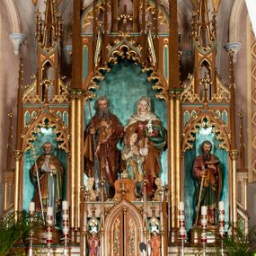 Zdjęcie nr 1: Nastawa ołtarzowa architektoniczna, jednokondygnacyjna, trójosiowa, ze zwieńczeniem. Ołtarz drewniany, skrzyniowy, mensa drewniana z marmurowym portatylem. Antepedium dekorowane czterem blendami, z czworoliściem z monogramem IHS w centrum. Tabernakulum w formie prostopadłościanu, dwukondygnacyjne, ze zwieńczeniem, na szerokiej podstawie. W dolnej kondygnacji dwoje drzwi dekorowanych ostrołukowymi blendami i przedzielonych służką. Wyżej tron wystawienia trójosiowy, w postaci trzech nisz zamkniętych łukiem ostrym, ujętych służkami dźwigającymi pinakle. Oś środkowa wyższa, z dwuskrzydłowymi drzwiczkami przedzielonymi służką i dekorowanymi płaskorzeźbioną winną latoroślą z kłosami zbóż. W niszach bocznych figury adorujących aniołów. Całość zwieńczona postumentem na relikwie. Retabulum ołtarzowe w postaci trzech nisz zamkniętych łukami ostrymi z ażurowym fryzem arkadkowym, dekorowanym po bokach blendami; osie wydzielone służkami, podwójnymi w osi środkowej, dźwigającymi pinakle z żabkami i kwiatonami. Osie zwieńczone ażurowymi wieżyczkami przeprutymi łukami trójlistnymi ostrymi, których pierwszą kondygnację kończy łuk odwrócony,  dekorowany pinaklami i żabkami, zwieńczony kwiatonem. Wieżyczki ujmują spływy z żabkami. Predella zdobiona blendami. W centralnej niszy grupa rzeźbiarska Rodziny Marii, w bocznych figury św. Piotra po lewej i św. Pawła po prawej stronie. Ołtarz w kolorze ciemnego drewna, blendy i nisze polichromowane na niebiesko i czerwono, profile, detale i ornamenty złocone. 