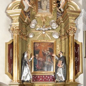 Zdjęcie nr 1: Nastawa ołtarzowa jednokondygnacyjna, jednoosiowa, ze zwieńczeniem i uszakami ustawiona na wysokim, dwudzielnym cokole. Przed nim prostopadłościenna mensa ołtarzowa z malowanym antepedium w kształcie leżącego prostokąta z przedstawieniem Ucieczki do Egiptu wzorowanym na kompozycji Giotta di Bondone. Na mensie prostopadłościenne tabernakulum zwieńczone gzymsem z drzwiczkami w kształcie stojącego prostokąta zamkniętego łukiem pełnym dekorowanymi kielichem z hostią. Kondygnacja nastawy flankowana jest przez ustawione skośnie do zewnątrz, zdwojone filary i stojące przed nimi, pozłacane kolumny o głowicach kompozytowych. W części centralnej znajduje się wnęka otoczona złotą, profilowaną ramą z rokokowym ornamentem, a w niej obraz Matki Boskiej z Dzieciątkiem, wymiennie ze sceną Zwiastowania, adorowany przez dwie flankujące go rzeźby – świętej zakonnicy po lewej i świętego zakonnika z księgą po prawej stronie. Poniżej pola obrazowego rama w kształcie leżącego prostokąta, po dwóch stronach kondygnacji uszaki w formie gablot w kształcie zbliżonym do trapezu, o wklęsło-wypukłych bokach. Wszystkie trzy wypełniają wota dziękczynne należące do obrazu Matki Boskiej. Kolumny i filary dźwigają belkowanie z rocaille'owym ornamentem na fryzie, zakończone mocno wysuniętym gzymsem, na którym umieszczono fragmenty przerwanego przyczółka. Na nim posadowiono putta trzymające kartusze, z napisami: „AVE” po lewej stronie i „MARIA” po prawej. Nad polem kondygnacji, na wysokości belkowania i gzymsu, znajduje się rzeźba gołębicy Ducha Świętego otoczona złotymi promieniami i czterema obłokami. Zwieńczenie zamknięte łukiem nadwieszonym mieści obraz z przedstawieniem Matki Boskiej Niepokalanie Poczętej w złotej profilowanej ramie, otoczony z trzech stron bujnym rocaille’owym ornamentem. Całość wieńczy kartusz utworzony z ornamentu rocaille’owego z monogramem maryjnym. Struktura polichromowana w imitacje marmoryzacji w kolorze zielonym, profile, detale i ornamenty złocone i srebrzone. 