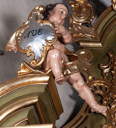 Zdjęcie nr 24: Retabulum jednokondygnacyjne, trójosiowe ze zwieńczeniem i bramkami. Mensa ołtarzowa z malowanym antepedium przedstawiającym scenę Ostatniej Wieczerzy według Leonarda da Vinci. Na mensie ustawione pozłacane tabernakulum w formie prostopadłościennej z częścią środkową w ozdobnej oprawie utworzonej przez dwa ukośnie dostawione filary ze spływami wolutowymi. Między nimi wypukłe w dolnej części drzwiczki dekorowane kielichem z hostią ponad kiśćmi winogron i między kłosami zbóż. Powyżej nisza konchowa wypełniona glorią, której koncha ozdobiona jest muszlą z rocaille’owym grzebieniem. Na wolutach osadzone adorujące krzyż putta. Część centralna nastawy flankowana kolumnami z głowicami jońskimi i ornamentem rokokowym. W polu w profilowanej złotej ramie przedstawienie koronacji Marii przez Trójcę Świętą. Drewniana konstrukcja skrzydeł bocznych tworzy ramę dla dwóch rzeźb ustawionych na bramkach, na odcinkach gzymsu rozszerzających się ku górze, które tworzą cokoły ozdobione w dolnej części rokokową muszlą. Po prawej stronie znajduje się rzeźba przedstawiająca św. Stanisława z Piotrowinem, po lewej św. Wojciecha. Obie rzeźby biskupów są tej samej wielkości, wypełniają prześwity w bocznych skrzydłach, w tle ozdobionych rocaille’owym ornamentem. Zewnętrzne płaszczyzny skrzydeł bocznych zdobi złota winorośl, a wewnętrzne ornament roślinny z motywem kwiatowym. Na kolumnach ustawionych na niewielkich cokołach wspiera się przełamane belkowanie zakończone gzymsem dźwigającym odcinkowy przyczółek z profilowaniem zakończonym wolutami. Na wysokości belkowania znajduje się płaskorzeźba przedstawiająca Boga Ojca i Ducha Świętego pod postacią gołębicy, wyłaniających się ze srebrnych obłoków; postacie otoczone są złotymi promieniami. Na bocznych osiach, analogicznie pojawiają się srebrne chmury o wolutowych kształtach, flankowane przez anielskie główki. Zwieńczenie rozszerza się ku górze i jest zamknięte łukiem nadwieszonym; znajduje się w nim obraz przedstawiający św. Floriana w profilowanej, złoconej wklęsło-wypukłej ramie. Całość zwieńczona kartuszem utworzonym z ornamentu rocaille’owego. Struktura polichromowana imitacją marmoryzacji w kolorze szarym i zielonym, fryzy i gzymsy bordowe i ciemnozielone, profile, ornamenty, kolumny złocone, dekoracje złocone i srebrzone. 