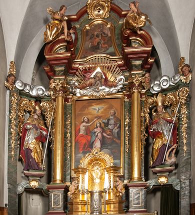 Zdjęcie nr 1: Retabulum jednokondygnacyjne, trójosiowe ze zwieńczeniem i bramkami. Mensa ołtarzowa z malowanym antepedium przedstawiającym scenę Ostatniej Wieczerzy według Leonarda da Vinci. Na mensie ustawione pozłacane tabernakulum w formie prostopadłościennej z częścią środkową w ozdobnej oprawie utworzonej przez dwa ukośnie dostawione filary ze spływami wolutowymi. Między nimi wypukłe w dolnej części drzwiczki dekorowane kielichem z hostią ponad kiśćmi winogron i między kłosami zbóż. Powyżej nisza konchowa wypełniona glorią, której koncha ozdobiona jest muszlą z rocaille’owym grzebieniem. Na wolutach osadzone adorujące krzyż putta. Część centralna nastawy flankowana kolumnami z głowicami jońskimi i ornamentem rokokowym. W polu w profilowanej złotej ramie przedstawienie koronacji Marii przez Trójcę Świętą. Drewniana konstrukcja skrzydeł bocznych tworzy ramę dla dwóch rzeźb ustawionych na bramkach, na odcinkach gzymsu rozszerzających się ku górze, które tworzą cokoły ozdobione w dolnej części rokokową muszlą. Po prawej stronie znajduje się rzeźba przedstawiająca św. Stanisława z Piotrowinem, po lewej św. Wojciecha. Obie rzeźby biskupów są tej samej wielkości, wypełniają prześwity w bocznych skrzydłach, w tle ozdobionych rocaille’owym ornamentem. Zewnętrzne płaszczyzny skrzydeł bocznych zdobi złota winorośl, a wewnętrzne ornament roślinny z motywem kwiatowym. Na kolumnach ustawionych na niewielkich cokołach wspiera się przełamane belkowanie zakończone gzymsem dźwigającym odcinkowy przyczółek z profilowaniem zakończonym wolutami. Na wysokości belkowania znajduje się płaskorzeźba przedstawiająca Boga Ojca i Ducha Świętego pod postacią gołębicy, wyłaniających się ze srebrnych obłoków; postacie otoczone są złotymi promieniami. Na bocznych osiach, analogicznie pojawiają się srebrne chmury o wolutowych kształtach, flankowane przez anielskie główki. Zwieńczenie rozszerza się ku górze i jest zamknięte łukiem nadwieszonym; znajduje się w nim obraz przedstawiający św. Floriana w profilowanej, złoconej wklęsło-wypukłej ramie. Całość zwieńczona kartuszem utworzonym z ornamentu rocaille’owego. Struktura polichromowana imitacją marmoryzacji w kolorze szarym i zielonym, fryzy i gzymsy bordowe i ciemnozielone, profile, ornamenty, kolumny złocone, dekoracje złocone i srebrzone. 