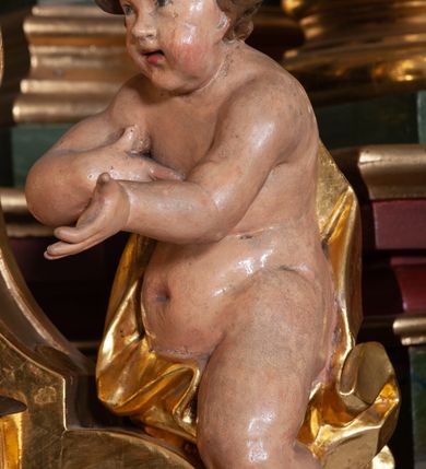 Zdjęcie nr 55: Retabulum jednokondygnacyjne, trójosiowe ze zwieńczeniem i bramkami. Mensa ołtarzowa z malowanym antepedium przedstawiającym scenę Ostatniej Wieczerzy według Leonarda da Vinci. Na mensie ustawione pozłacane tabernakulum w formie prostopadłościennej z częścią środkową w ozdobnej oprawie utworzonej przez dwa ukośnie dostawione filary ze spływami wolutowymi. Między nimi wypukłe w dolnej części drzwiczki dekorowane kielichem z hostią ponad kiśćmi winogron i między kłosami zbóż. Powyżej nisza konchowa wypełniona glorią, której koncha ozdobiona jest muszlą z rocaille’owym grzebieniem. Na wolutach osadzone adorujące krzyż putta. Część centralna nastawy flankowana kolumnami z głowicami jońskimi i ornamentem rokokowym. W polu w profilowanej złotej ramie przedstawienie koronacji Marii przez Trójcę Świętą. Drewniana konstrukcja skrzydeł bocznych tworzy ramę dla dwóch rzeźb ustawionych na bramkach, na odcinkach gzymsu rozszerzających się ku górze, które tworzą cokoły ozdobione w dolnej części rokokową muszlą. Po prawej stronie znajduje się rzeźba przedstawiająca św. Stanisława z Piotrowinem, po lewej św. Wojciecha. Obie rzeźby biskupów są tej samej wielkości, wypełniają prześwity w bocznych skrzydłach, w tle ozdobionych rocaille’owym ornamentem. Zewnętrzne płaszczyzny skrzydeł bocznych zdobi złota winorośl, a wewnętrzne ornament roślinny z motywem kwiatowym. Na kolumnach ustawionych na niewielkich cokołach wspiera się przełamane belkowanie zakończone gzymsem dźwigającym odcinkowy przyczółek z profilowaniem zakończonym wolutami. Na wysokości belkowania znajduje się płaskorzeźba przedstawiająca Boga Ojca i Ducha Świętego pod postacią gołębicy, wyłaniających się ze srebrnych obłoków; postacie otoczone są złotymi promieniami. Na bocznych osiach, analogicznie pojawiają się srebrne chmury o wolutowych kształtach, flankowane przez anielskie główki. Zwieńczenie rozszerza się ku górze i jest zamknięte łukiem nadwieszonym; znajduje się w nim obraz przedstawiający św. Floriana w profilowanej, złoconej wklęsło-wypukłej ramie. Całość zwieńczona kartuszem utworzonym z ornamentu rocaille’owego. Struktura polichromowana imitacją marmoryzacji w kolorze szarym i zielonym, fryzy i gzymsy bordowe i ciemnozielone, profile, ornamenty, kolumny złocone, dekoracje złocone i srebrzone. 