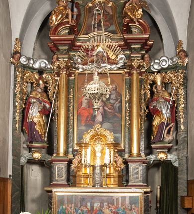 Zdjęcie nr 2: Retabulum jednokondygnacyjne, trójosiowe ze zwieńczeniem i bramkami. Mensa ołtarzowa z malowanym antepedium przedstawiającym scenę Ostatniej Wieczerzy według Leonarda da Vinci. Na mensie ustawione pozłacane tabernakulum w formie prostopadłościennej z częścią środkową w ozdobnej oprawie utworzonej przez dwa ukośnie dostawione filary ze spływami wolutowymi. Między nimi wypukłe w dolnej części drzwiczki dekorowane kielichem z hostią ponad kiśćmi winogron i między kłosami zbóż. Powyżej nisza konchowa wypełniona glorią, której koncha ozdobiona jest muszlą z rocaille’owym grzebieniem. Na wolutach osadzone adorujące krzyż putta. Część centralna nastawy flankowana kolumnami z głowicami jońskimi i ornamentem rokokowym. W polu w profilowanej złotej ramie przedstawienie koronacji Marii przez Trójcę Świętą. Drewniana konstrukcja skrzydeł bocznych tworzy ramę dla dwóch rzeźb ustawionych na bramkach, na odcinkach gzymsu rozszerzających się ku górze, które tworzą cokoły ozdobione w dolnej części rokokową muszlą. Po prawej stronie znajduje się rzeźba przedstawiająca św. Stanisława z Piotrowinem, po lewej św. Wojciecha. Obie rzeźby biskupów są tej samej wielkości, wypełniają prześwity w bocznych skrzydłach, w tle ozdobionych rocaille’owym ornamentem. Zewnętrzne płaszczyzny skrzydeł bocznych zdobi złota winorośl, a wewnętrzne ornament roślinny z motywem kwiatowym. Na kolumnach ustawionych na niewielkich cokołach wspiera się przełamane belkowanie zakończone gzymsem dźwigającym odcinkowy przyczółek z profilowaniem zakończonym wolutami. Na wysokości belkowania znajduje się płaskorzeźba przedstawiająca Boga Ojca i Ducha Świętego pod postacią gołębicy, wyłaniających się ze srebrnych obłoków; postacie otoczone są złotymi promieniami. Na bocznych osiach, analogicznie pojawiają się srebrne chmury o wolutowych kształtach, flankowane przez anielskie główki. Zwieńczenie rozszerza się ku górze i jest zamknięte łukiem nadwieszonym; znajduje się w nim obraz przedstawiający św. Floriana w profilowanej, złoconej wklęsło-wypukłej ramie. Całość zwieńczona kartuszem utworzonym z ornamentu rocaille’owego. Struktura polichromowana imitacją marmoryzacji w kolorze szarym i zielonym, fryzy i gzymsy bordowe i ciemnozielone, profile, ornamenty, kolumny złocone, dekoracje złocone i srebrzone. 