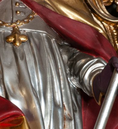 Zdjęcie nr 15: Retabulum jednokondygnacyjne, trójosiowe ze zwieńczeniem i bramkami. Mensa ołtarzowa z malowanym antepedium przedstawiającym scenę Ostatniej Wieczerzy według Leonarda da Vinci. Na mensie ustawione pozłacane tabernakulum w formie prostopadłościennej z częścią środkową w ozdobnej oprawie utworzonej przez dwa ukośnie dostawione filary ze spływami wolutowymi. Między nimi wypukłe w dolnej części drzwiczki dekorowane kielichem z hostią ponad kiśćmi winogron i między kłosami zbóż. Powyżej nisza konchowa wypełniona glorią, której koncha ozdobiona jest muszlą z rocaille’owym grzebieniem. Na wolutach osadzone adorujące krzyż putta. Część centralna nastawy flankowana kolumnami z głowicami jońskimi i ornamentem rokokowym. W polu w profilowanej złotej ramie przedstawienie koronacji Marii przez Trójcę Świętą. Drewniana konstrukcja skrzydeł bocznych tworzy ramę dla dwóch rzeźb ustawionych na bramkach, na odcinkach gzymsu rozszerzających się ku górze, które tworzą cokoły ozdobione w dolnej części rokokową muszlą. Po prawej stronie znajduje się rzeźba przedstawiająca św. Stanisława z Piotrowinem, po lewej św. Wojciecha. Obie rzeźby biskupów są tej samej wielkości, wypełniają prześwity w bocznych skrzydłach, w tle ozdobionych rocaille’owym ornamentem. Zewnętrzne płaszczyzny skrzydeł bocznych zdobi złota winorośl, a wewnętrzne ornament roślinny z motywem kwiatowym. Na kolumnach ustawionych na niewielkich cokołach wspiera się przełamane belkowanie zakończone gzymsem dźwigającym odcinkowy przyczółek z profilowaniem zakończonym wolutami. Na wysokości belkowania znajduje się płaskorzeźba przedstawiająca Boga Ojca i Ducha Świętego pod postacią gołębicy, wyłaniających się ze srebrnych obłoków; postacie otoczone są złotymi promieniami. Na bocznych osiach, analogicznie pojawiają się srebrne chmury o wolutowych kształtach, flankowane przez anielskie główki. Zwieńczenie rozszerza się ku górze i jest zamknięte łukiem nadwieszonym; znajduje się w nim obraz przedstawiający św. Floriana w profilowanej, złoconej wklęsło-wypukłej ramie. Całość zwieńczona kartuszem utworzonym z ornamentu rocaille’owego. Struktura polichromowana imitacją marmoryzacji w kolorze szarym i zielonym, fryzy i gzymsy bordowe i ciemnozielone, profile, ornamenty, kolumny złocone, dekoracje złocone i srebrzone. 