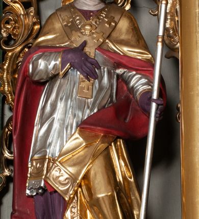 Zdjęcie nr 5: Retabulum jednokondygnacyjne, trójosiowe ze zwieńczeniem i bramkami. Mensa ołtarzowa z malowanym antepedium przedstawiającym scenę Ostatniej Wieczerzy według Leonarda da Vinci. Na mensie ustawione pozłacane tabernakulum w formie prostopadłościennej z częścią środkową w ozdobnej oprawie utworzonej przez dwa ukośnie dostawione filary ze spływami wolutowymi. Między nimi wypukłe w dolnej części drzwiczki dekorowane kielichem z hostią ponad kiśćmi winogron i między kłosami zbóż. Powyżej nisza konchowa wypełniona glorią, której koncha ozdobiona jest muszlą z rocaille’owym grzebieniem. Na wolutach osadzone adorujące krzyż putta. Część centralna nastawy flankowana kolumnami z głowicami jońskimi i ornamentem rokokowym. W polu w profilowanej złotej ramie przedstawienie koronacji Marii przez Trójcę Świętą. Drewniana konstrukcja skrzydeł bocznych tworzy ramę dla dwóch rzeźb ustawionych na bramkach, na odcinkach gzymsu rozszerzających się ku górze, które tworzą cokoły ozdobione w dolnej części rokokową muszlą. Po prawej stronie znajduje się rzeźba przedstawiająca św. Stanisława z Piotrowinem, po lewej św. Wojciecha. Obie rzeźby biskupów są tej samej wielkości, wypełniają prześwity w bocznych skrzydłach, w tle ozdobionych rocaille’owym ornamentem. Zewnętrzne płaszczyzny skrzydeł bocznych zdobi złota winorośl, a wewnętrzne ornament roślinny z motywem kwiatowym. Na kolumnach ustawionych na niewielkich cokołach wspiera się przełamane belkowanie zakończone gzymsem dźwigającym odcinkowy przyczółek z profilowaniem zakończonym wolutami. Na wysokości belkowania znajduje się płaskorzeźba przedstawiająca Boga Ojca i Ducha Świętego pod postacią gołębicy, wyłaniających się ze srebrnych obłoków; postacie otoczone są złotymi promieniami. Na bocznych osiach, analogicznie pojawiają się srebrne chmury o wolutowych kształtach, flankowane przez anielskie główki. Zwieńczenie rozszerza się ku górze i jest zamknięte łukiem nadwieszonym; znajduje się w nim obraz przedstawiający św. Floriana w profilowanej, złoconej wklęsło-wypukłej ramie. Całość zwieńczona kartuszem utworzonym z ornamentu rocaille’owego. Struktura polichromowana imitacją marmoryzacji w kolorze szarym i zielonym, fryzy i gzymsy bordowe i ciemnozielone, profile, ornamenty, kolumny złocone, dekoracje złocone i srebrzone. 