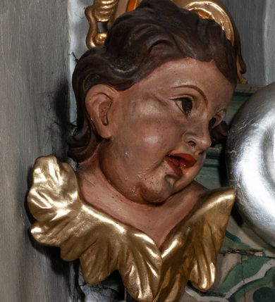 Zdjęcie nr 49: Retabulum jednokondygnacyjne, trójosiowe ze zwieńczeniem i bramkami. Mensa ołtarzowa z malowanym antepedium przedstawiającym scenę Ostatniej Wieczerzy według Leonarda da Vinci. Na mensie ustawione pozłacane tabernakulum w formie prostopadłościennej z częścią środkową w ozdobnej oprawie utworzonej przez dwa ukośnie dostawione filary ze spływami wolutowymi. Między nimi wypukłe w dolnej części drzwiczki dekorowane kielichem z hostią ponad kiśćmi winogron i między kłosami zbóż. Powyżej nisza konchowa wypełniona glorią, której koncha ozdobiona jest muszlą z rocaille’owym grzebieniem. Na wolutach osadzone adorujące krzyż putta. Część centralna nastawy flankowana kolumnami z głowicami jońskimi i ornamentem rokokowym. W polu w profilowanej złotej ramie przedstawienie koronacji Marii przez Trójcę Świętą. Drewniana konstrukcja skrzydeł bocznych tworzy ramę dla dwóch rzeźb ustawionych na bramkach, na odcinkach gzymsu rozszerzających się ku górze, które tworzą cokoły ozdobione w dolnej części rokokową muszlą. Po prawej stronie znajduje się rzeźba przedstawiająca św. Stanisława z Piotrowinem, po lewej św. Wojciecha. Obie rzeźby biskupów są tej samej wielkości, wypełniają prześwity w bocznych skrzydłach, w tle ozdobionych rocaille’owym ornamentem. Zewnętrzne płaszczyzny skrzydeł bocznych zdobi złota winorośl, a wewnętrzne ornament roślinny z motywem kwiatowym. Na kolumnach ustawionych na niewielkich cokołach wspiera się przełamane belkowanie zakończone gzymsem dźwigającym odcinkowy przyczółek z profilowaniem zakończonym wolutami. Na wysokości belkowania znajduje się płaskorzeźba przedstawiająca Boga Ojca i Ducha Świętego pod postacią gołębicy, wyłaniających się ze srebrnych obłoków; postacie otoczone są złotymi promieniami. Na bocznych osiach, analogicznie pojawiają się srebrne chmury o wolutowych kształtach, flankowane przez anielskie główki. Zwieńczenie rozszerza się ku górze i jest zamknięte łukiem nadwieszonym; znajduje się w nim obraz przedstawiający św. Floriana w profilowanej, złoconej wklęsło-wypukłej ramie. Całość zwieńczona kartuszem utworzonym z ornamentu rocaille’owego. Struktura polichromowana imitacją marmoryzacji w kolorze szarym i zielonym, fryzy i gzymsy bordowe i ciemnozielone, profile, ornamenty, kolumny złocone, dekoracje złocone i srebrzone. 