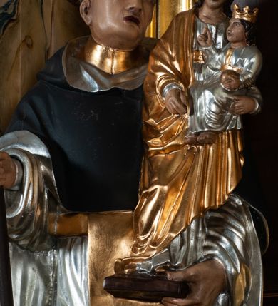 Zdjęcie nr 4: Rzeźba pełna na cokole. Święty Jacek wyobrażony w całej postaci, stojący frontalnie, w kontrapoście, z lewą nogą wysuniętą do przodu. Obie ręce zgięte w łokciach, w prawej trzyma kij, w lewej figurkę Matki Boskiej z Dzieciątkiem w srebrnych i złotych szatach. Twarz podłużna, oczy małe, nos prosty, usta szerokie, ciemnoczerwone. Głowa otoczona krótkimi, brązowymi włosami z wyciętą tonsurą. Święty ubrany jest w srebrny habit ze złotym szkaplerzem i czarny płaszcz z kapturem, spod ubrania widoczne czubki czarnych butów. Polichromia w odsłoniętych partiach karnacji traktowana naturalistyczne. 