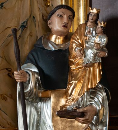 Zdjęcie nr 1: Rzeźba pełna na cokole. Święty Jacek wyobrażony w całej postaci, stojący frontalnie, w kontrapoście, z lewą nogą wysuniętą do przodu. Obie ręce zgięte w łokciach, w prawej trzyma kij, w lewej figurkę Matki Boskiej z Dzieciątkiem w srebrnych i złotych szatach. Twarz podłużna, oczy małe, nos prosty, usta szerokie, ciemnoczerwone. Głowa otoczona krótkimi, brązowymi włosami z wyciętą tonsurą. Święty ubrany jest w srebrny habit ze złotym szkaplerzem i czarny płaszcz z kapturem, spod ubrania widoczne czubki czarnych butów. Polichromia w odsłoniętych partiach karnacji traktowana naturalistyczne. 