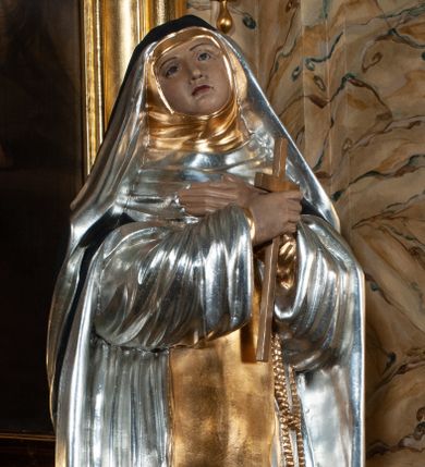 Zdjęcie nr 1: Rzeźba pełnoplastyczna, całopostaciowa, na cokole. Święta Katarzyna została ukazana frontalnie, w kontrapoście, z ciężarem na prawej nodze i głową przechyloną na prawo. Obie ręce krzyżuje na piersiach, w prawej trzyma krucyfiks, przez lewą ma przewieszony różaniec. Święta ma owalną twarz, ciemne spoglądające do góry oczy, wąskie brwi, prosty nos oraz wąskie, czerwone usta. Jest ubrana w srebrny habit dominikański, złoty szkaplerz oraz długi, czarny płaszcz, na głowie ma czarny welon. Polichromia w partiach ciała naturalistyczna.