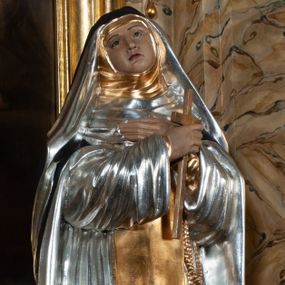 Zdjęcie nr 1: Rzeźba pełnoplastyczna, całopostaciowa, na cokole. Święta Katarzyna została ukazana frontalnie, w kontrapoście, z ciężarem na prawej nodze i głową przechyloną na prawo. Obie ręce krzyżuje na piersiach, w prawej trzyma krucyfiks, przez lewą ma przewieszony różaniec. Święta ma owalną twarz, ciemne spoglądające do góry oczy, wąskie brwi, prosty nos oraz wąskie, czerwone usta. Jest ubrana w srebrny habit dominikański, złoty szkaplerz oraz długi, czarny płaszcz, na głowie ma czarny welon. Polichromia w partiach ciała naturalistyczna.