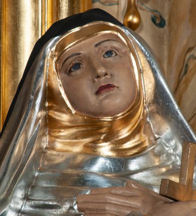 Zdjęcie nr 4: Rzeźba pełnoplastyczna, całopostaciowa, na cokole. Święta Katarzyna została ukazana frontalnie, w kontrapoście, z ciężarem na prawej nodze i głową przechyloną na prawo. Obie ręce krzyżuje na piersiach, w prawej trzyma krucyfiks, przez lewą ma przewieszony różaniec. Święta ma owalną twarz, ciemne spoglądające do góry oczy, wąskie brwi, prosty nos oraz wąskie, czerwone usta. Jest ubrana w srebrny habit dominikański, złoty szkaplerz oraz długi, czarny płaszcz, na głowie ma czarny welon. Polichromia w partiach ciała naturalistyczna.