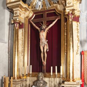 Zdjęcie nr 1: Ołtarz jednokondygnacyjny, jednoosiowy, na wysokim cokole, ze zwieńczeniem w formie glorii. Mensa ołtarzowa w kształcie prostopadłościanu, antepedium w postaci leżącego prostokąta, tkane, dekorowane rzędem maków w dolnej partii. Kondygnacja nastawy flankowana przez zwielokrotnione pilastry, ozdobione z zewnętrznych stron ornamentami roślinnymi i wysuniętymi przed nie kolumnami z głowicami kompozytowymi, ozdobionymi wolutami i liśćmi akantu. Kolumny i pilastry ustawione na wysokim cokole dekorowanym płycinami, dźwigają rozbudowane belkowanie, w pasie fryzu dekorowane rozetami. Belkowanie przełamuje się nad zwielokrotnionymi pilastrami i kolumnami i podtrzymuje fragment przerwanego przyczółka, na którym siedzą dwa putta. W polu znajduje się wnęka w kształcie stojącego prostokąta o górnych narożach wklęsłych, w której umieszczono krucyfiks. Zwieńczenie tworzy gloria promienista z centralnie umieszczonym okiem Opatrzności w otoku z obłoków i główek anielskich. Struktura polichromowana, marmoryzowana w odcieniu kremowym, kolumny, ornamenty i profile złocone, płyciny bordowe, gloria srebrzona i złocona.  