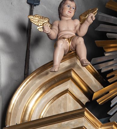 Zdjęcie nr 2: Ołtarz jednokondygnacyjny, jednoosiowy, na wysokim cokole, ze zwieńczeniem w formie glorii. Mensa ołtarzowa w kształcie prostopadłościanu, antepedium w postaci leżącego prostokąta, tkane, dekorowane rzędem maków w dolnej partii. Kondygnacja nastawy flankowana przez zwielokrotnione pilastry, ozdobione z zewnętrznych stron ornamentami roślinnymi i wysuniętymi przed nie kolumnami z głowicami kompozytowymi, ozdobionymi wolutami i liśćmi akantu. Kolumny i pilastry ustawione na wysokim cokole dekorowanym płycinami, dźwigają rozbudowane belkowanie, w pasie fryzu dekorowane rozetami. Belkowanie przełamuje się nad zwielokrotnionymi pilastrami i kolumnami i podtrzymuje fragment przerwanego przyczółka, na którym siedzą dwa putta. W polu znajduje się wnęka w kształcie stojącego prostokąta o górnych narożach wklęsłych, w której umieszczono krucyfiks. Zwieńczenie tworzy gloria promienista z centralnie umieszczonym okiem Opatrzności w otoku z obłoków i główek anielskich. Struktura polichromowana, marmoryzowana w odcieniu kremowym, kolumny, ornamenty i profile złocone, płyciny bordowe, gloria srebrzona i złocona.  