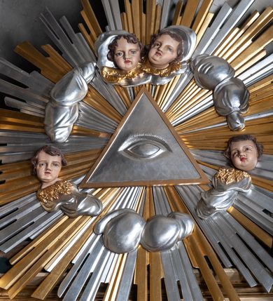 Zdjęcie nr 12: Ołtarz jednokondygnacyjny, jednoosiowy, na wysokim cokole, ze zwieńczeniem w formie glorii. Mensa ołtarzowa w kształcie prostopadłościanu, antepedium w postaci leżącego prostokąta, tkane, dekorowane rzędem maków w dolnej partii. Kondygnacja nastawy flankowana przez zwielokrotnione pilastry, ozdobione z zewnętrznych stron ornamentami roślinnymi i wysuniętymi przed nie kolumnami z głowicami kompozytowymi, ozdobionymi wolutami i liśćmi akantu. Kolumny i pilastry ustawione na wysokim cokole dekorowanym płycinami, dźwigają rozbudowane belkowanie, w pasie fryzu dekorowane rozetami. Belkowanie przełamuje się nad zwielokrotnionymi pilastrami i kolumnami i podtrzymuje fragment przerwanego przyczółka, na którym siedzą dwa putta. W polu znajduje się wnęka w kształcie stojącego prostokąta o górnych narożach wklęsłych, w której umieszczono krucyfiks. Zwieńczenie tworzy gloria promienista z centralnie umieszczonym okiem Opatrzności w otoku z obłoków i główek anielskich. Struktura polichromowana, marmoryzowana w odcieniu kremowym, kolumny, ornamenty i profile złocone, płyciny bordowe, gloria srebrzona i złocona.  