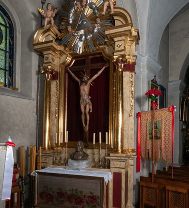 Zdjęcie nr 16: Ołtarz jednokondygnacyjny, jednoosiowy, na wysokim cokole, ze zwieńczeniem w formie glorii. Mensa ołtarzowa w kształcie prostopadłościanu, antepedium w postaci leżącego prostokąta, tkane, dekorowane rzędem maków w dolnej partii. Kondygnacja nastawy flankowana przez zwielokrotnione pilastry, ozdobione z zewnętrznych stron ornamentami roślinnymi i wysuniętymi przed nie kolumnami z głowicami kompozytowymi, ozdobionymi wolutami i liśćmi akantu. Kolumny i pilastry ustawione na wysokim cokole dekorowanym płycinami, dźwigają rozbudowane belkowanie, w pasie fryzu dekorowane rozetami. Belkowanie przełamuje się nad zwielokrotnionymi pilastrami i kolumnami i podtrzymuje fragment przerwanego przyczółka, na którym siedzą dwa putta. W polu znajduje się wnęka w kształcie stojącego prostokąta o górnych narożach wklęsłych, w której umieszczono krucyfiks. Zwieńczenie tworzy gloria promienista z centralnie umieszczonym okiem Opatrzności w otoku z obłoków i główek anielskich. Struktura polichromowana, marmoryzowana w odcieniu kremowym, kolumny, ornamenty i profile złocone, płyciny bordowe, gloria srebrzona i złocona.  