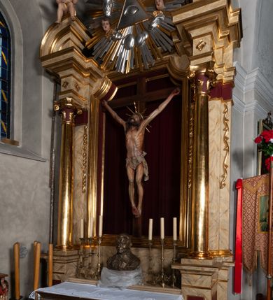 Zdjęcie nr 15: Ołtarz jednokondygnacyjny, jednoosiowy, na wysokim cokole, ze zwieńczeniem w formie glorii. Mensa ołtarzowa w kształcie prostopadłościanu, antepedium w postaci leżącego prostokąta, tkane, dekorowane rzędem maków w dolnej partii. Kondygnacja nastawy flankowana przez zwielokrotnione pilastry, ozdobione z zewnętrznych stron ornamentami roślinnymi i wysuniętymi przed nie kolumnami z głowicami kompozytowymi, ozdobionymi wolutami i liśćmi akantu. Kolumny i pilastry ustawione na wysokim cokole dekorowanym płycinami, dźwigają rozbudowane belkowanie, w pasie fryzu dekorowane rozetami. Belkowanie przełamuje się nad zwielokrotnionymi pilastrami i kolumnami i podtrzymuje fragment przerwanego przyczółka, na którym siedzą dwa putta. W polu znajduje się wnęka w kształcie stojącego prostokąta o górnych narożach wklęsłych, w której umieszczono krucyfiks. Zwieńczenie tworzy gloria promienista z centralnie umieszczonym okiem Opatrzności w otoku z obłoków i główek anielskich. Struktura polichromowana, marmoryzowana w odcieniu kremowym, kolumny, ornamenty i profile złocone, płyciny bordowe, gloria srebrzona i złocona.  