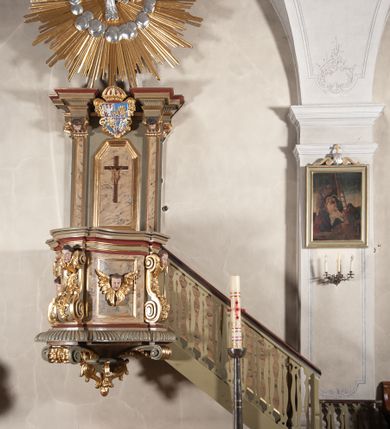 Zdjęcie nr 1: Ambona przyścienna, wisząca, dostępna od strony prezbiterium. Kosz na planie wklęsło-wypukłym, na  zwężającym się cokole dekorowanym liśćmi. U spodu podwieszone dekorowane rocaille’m woluty podtrzymujące szyszkę. Ścianki kosza wklęsłe, zdobione  płycinami wypełnionymi główkami anielskimi, a ścięte naroża wolutami z rocaille’m i główkami anielskimi. Kosz zamknięty parapetem w formie belkowania, wyłamanego na narożach. Z prawej strony do kosza prowadzą schody z ażurową balustradą wyciętą w pionowe, fantazyjne kształty, z poręczą. Zaplecek w kształcie stojącego prostokąta flankowany pilastrami wypełnionymi płycinami z głowicami utworzonymi z wolut i główek anielskich, podtrzymującymi fragmenty pełnego, wyłamanego na ich osiach belkowania. W polu płycina w kształcie stojącego prostokąta o ściętych górnych narożach z krucyfiksem. Nad nią, między fragmentami belkowania pięciopolowy herb Wazów zwieńczony koroną. Ponad zapleckiem płaskorzeźbiona gołębica Ducha Świętego w otoku z obłoków na tle dużych rozmiarów glorii promienistej. 
Struktura polichromowana w kolorze zielonym; płyciny marmoryzowane w odcieniu jasnego brązu; profilowania brązowe, detale, ornamenty, gloria złocone, gołębica i obłoki srebrzone. 
