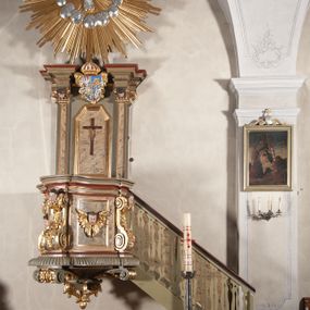 Zdjęcie nr 1: Ambona przyścienna, wisząca, dostępna od strony prezbiterium. Kosz na planie wklęsło-wypukłym, na  zwężającym się cokole dekorowanym liśćmi. U spodu podwieszone dekorowane rocaille’m woluty podtrzymujące szyszkę. Ścianki kosza wklęsłe, zdobione  płycinami wypełnionymi główkami anielskimi, a ścięte naroża wolutami z rocaille’m i główkami anielskimi. Kosz zamknięty parapetem w formie belkowania, wyłamanego na narożach. Z prawej strony do kosza prowadzą schody z ażurową balustradą wyciętą w pionowe, fantazyjne kształty, z poręczą. Zaplecek w kształcie stojącego prostokąta flankowany pilastrami wypełnionymi płycinami z głowicami utworzonymi z wolut i główek anielskich, podtrzymującymi fragmenty pełnego, wyłamanego na ich osiach belkowania. W polu płycina w kształcie stojącego prostokąta o ściętych górnych narożach z krucyfiksem. Nad nią, między fragmentami belkowania pięciopolowy herb Wazów zwieńczony koroną. Ponad zapleckiem płaskorzeźbiona gołębica Ducha Świętego w otoku z obłoków na tle dużych rozmiarów glorii promienistej. 
Struktura polichromowana w kolorze zielonym; płyciny marmoryzowane w odcieniu jasnego brązu; profilowania brązowe, detale, ornamenty, gloria złocone, gołębica i obłoki srebrzone. 
