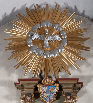 Zdjęcie nr 11: Ambona przyścienna, wisząca, dostępna od strony prezbiterium. Kosz na planie wklęsło-wypukłym, na  zwężającym się cokole dekorowanym liśćmi. U spodu podwieszone dekorowane rocaille’m woluty podtrzymujące szyszkę. Ścianki kosza wklęsłe, zdobione  płycinami wypełnionymi główkami anielskimi, a ścięte naroża wolutami z rocaille’m i główkami anielskimi. Kosz zamknięty parapetem w formie belkowania, wyłamanego na narożach. Z prawej strony do kosza prowadzą schody z ażurową balustradą wyciętą w pionowe, fantazyjne kształty, z poręczą. Zaplecek w kształcie stojącego prostokąta flankowany pilastrami wypełnionymi płycinami z głowicami utworzonymi z wolut i główek anielskich, podtrzymującymi fragmenty pełnego, wyłamanego na ich osiach belkowania. W polu płycina w kształcie stojącego prostokąta o ściętych górnych narożach z krucyfiksem. Nad nią, między fragmentami belkowania pięciopolowy herb Wazów zwieńczony koroną. Ponad zapleckiem płaskorzeźbiona gołębica Ducha Świętego w otoku z obłoków na tle dużych rozmiarów glorii promienistej. 
Struktura polichromowana w kolorze zielonym; płyciny marmoryzowane w odcieniu jasnego brązu; profilowania brązowe, detale, ornamenty, gloria złocone, gołębica i obłoki srebrzone. 
