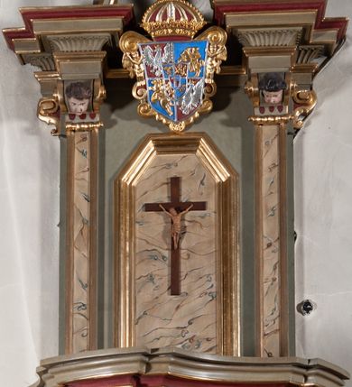 Zdjęcie nr 9: Ambona przyścienna, wisząca, dostępna od strony prezbiterium. Kosz na planie wklęsło-wypukłym, na  zwężającym się cokole dekorowanym liśćmi. U spodu podwieszone dekorowane rocaille’m woluty podtrzymujące szyszkę. Ścianki kosza wklęsłe, zdobione  płycinami wypełnionymi główkami anielskimi, a ścięte naroża wolutami z rocaille’m i główkami anielskimi. Kosz zamknięty parapetem w formie belkowania, wyłamanego na narożach. Z prawej strony do kosza prowadzą schody z ażurową balustradą wyciętą w pionowe, fantazyjne kształty, z poręczą. Zaplecek w kształcie stojącego prostokąta flankowany pilastrami wypełnionymi płycinami z głowicami utworzonymi z wolut i główek anielskich, podtrzymującymi fragmenty pełnego, wyłamanego na ich osiach belkowania. W polu płycina w kształcie stojącego prostokąta o ściętych górnych narożach z krucyfiksem. Nad nią, między fragmentami belkowania pięciopolowy herb Wazów zwieńczony koroną. Ponad zapleckiem płaskorzeźbiona gołębica Ducha Świętego w otoku z obłoków na tle dużych rozmiarów glorii promienistej. 
Struktura polichromowana w kolorze zielonym; płyciny marmoryzowane w odcieniu jasnego brązu; profilowania brązowe, detale, ornamenty, gloria złocone, gołębica i obłoki srebrzone. 
