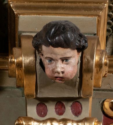 Zdjęcie nr 7: Ambona przyścienna, wisząca, dostępna od strony prezbiterium. Kosz na planie wklęsło-wypukłym, na  zwężającym się cokole dekorowanym liśćmi. U spodu podwieszone dekorowane rocaille’m woluty podtrzymujące szyszkę. Ścianki kosza wklęsłe, zdobione  płycinami wypełnionymi główkami anielskimi, a ścięte naroża wolutami z rocaille’m i główkami anielskimi. Kosz zamknięty parapetem w formie belkowania, wyłamanego na narożach. Z prawej strony do kosza prowadzą schody z ażurową balustradą wyciętą w pionowe, fantazyjne kształty, z poręczą. Zaplecek w kształcie stojącego prostokąta flankowany pilastrami wypełnionymi płycinami z głowicami utworzonymi z wolut i główek anielskich, podtrzymującymi fragmenty pełnego, wyłamanego na ich osiach belkowania. W polu płycina w kształcie stojącego prostokąta o ściętych górnych narożach z krucyfiksem. Nad nią, między fragmentami belkowania pięciopolowy herb Wazów zwieńczony koroną. Ponad zapleckiem płaskorzeźbiona gołębica Ducha Świętego w otoku z obłoków na tle dużych rozmiarów glorii promienistej. 
Struktura polichromowana w kolorze zielonym; płyciny marmoryzowane w odcieniu jasnego brązu; profilowania brązowe, detale, ornamenty, gloria złocone, gołębica i obłoki srebrzone. 
