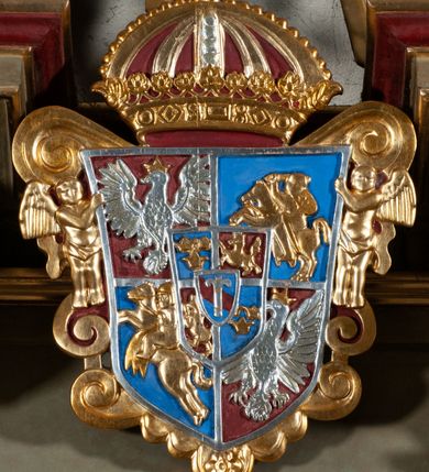 Zdjęcie nr 5: Ambona przyścienna, wisząca, dostępna od strony prezbiterium. Kosz na planie wklęsło-wypukłym, na  zwężającym się cokole dekorowanym liśćmi. U spodu podwieszone dekorowane rocaille’m woluty podtrzymujące szyszkę. Ścianki kosza wklęsłe, zdobione  płycinami wypełnionymi główkami anielskimi, a ścięte naroża wolutami z rocaille’m i główkami anielskimi. Kosz zamknięty parapetem w formie belkowania, wyłamanego na narożach. Z prawej strony do kosza prowadzą schody z ażurową balustradą wyciętą w pionowe, fantazyjne kształty, z poręczą. Zaplecek w kształcie stojącego prostokąta flankowany pilastrami wypełnionymi płycinami z głowicami utworzonymi z wolut i główek anielskich, podtrzymującymi fragmenty pełnego, wyłamanego na ich osiach belkowania. W polu płycina w kształcie stojącego prostokąta o ściętych górnych narożach z krucyfiksem. Nad nią, między fragmentami belkowania pięciopolowy herb Wazów zwieńczony koroną. Ponad zapleckiem płaskorzeźbiona gołębica Ducha Świętego w otoku z obłoków na tle dużych rozmiarów glorii promienistej. 
Struktura polichromowana w kolorze zielonym; płyciny marmoryzowane w odcieniu jasnego brązu; profilowania brązowe, detale, ornamenty, gloria złocone, gołębica i obłoki srebrzone. 
