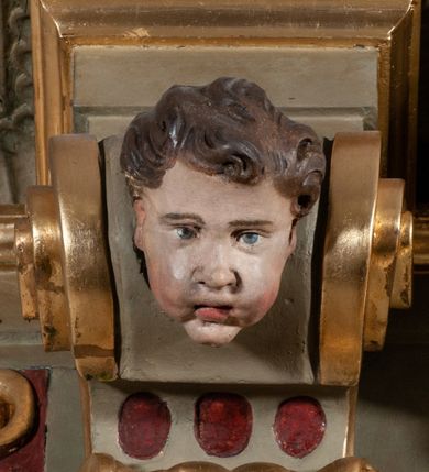 Zdjęcie nr 6: Ambona przyścienna, wisząca, dostępna od strony prezbiterium. Kosz na planie wklęsło-wypukłym, na  zwężającym się cokole dekorowanym liśćmi. U spodu podwieszone dekorowane rocaille’m woluty podtrzymujące szyszkę. Ścianki kosza wklęsłe, zdobione  płycinami wypełnionymi główkami anielskimi, a ścięte naroża wolutami z rocaille’m i główkami anielskimi. Kosz zamknięty parapetem w formie belkowania, wyłamanego na narożach. Z prawej strony do kosza prowadzą schody z ażurową balustradą wyciętą w pionowe, fantazyjne kształty, z poręczą. Zaplecek w kształcie stojącego prostokąta flankowany pilastrami wypełnionymi płycinami z głowicami utworzonymi z wolut i główek anielskich, podtrzymującymi fragmenty pełnego, wyłamanego na ich osiach belkowania. W polu płycina w kształcie stojącego prostokąta o ściętych górnych narożach z krucyfiksem. Nad nią, między fragmentami belkowania pięciopolowy herb Wazów zwieńczony koroną. Ponad zapleckiem płaskorzeźbiona gołębica Ducha Świętego w otoku z obłoków na tle dużych rozmiarów glorii promienistej. 
Struktura polichromowana w kolorze zielonym; płyciny marmoryzowane w odcieniu jasnego brązu; profilowania brązowe, detale, ornamenty, gloria złocone, gołębica i obłoki srebrzone. 
