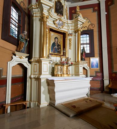 Zdjęcie nr 23: Ołtarz architektoniczny, drewniany, jednoosiowy, jednokondygnacyjny z bramkami. Mensa wąska, prostopadłościenna o ściankach wklęsło-wypukłych. Tabernakulum w kształcie prostopadłościennej skrzynki z przodu o linii wklęsło-wypukłej z uskokami. Ustawione jest na  wysokim cokole, flankowane parą szerokich, wklęsłych pilastrów, zdobionych ornamentem złożonym z przeplatających się wolut i kampanul. Ścianka frontowa wypukła, w polu prostokątne, metalowe drzwiczki, zdobione kiśćmi winogron i kłosami zbóż, pośrodku łaciński prosty krzyż. Całość zamknięta profilowanym gzymsem. Po bokach tabernakulum zwisy z kampanul, a na skrajach płaskorzeźbione uszy z liści akantu.  Do górnej krawędzi przybite gwoździem na trzech tulejach lampki oliwne. Nad tabernakulum tron wystawienia z rzeźbionymi w drewnie aniołkami na obłokach adorującymi krucyfiks. 

Retabulum ustawione na zdwojonym cokole, ujęte zwielokrotnionymi pilastrami toskańskimi i dwiema kolumnami kompozytowymi na wysokich cokołach, ustawionymi pod kątem i podtrzymującymi profilowane, przerwane belkowanie. Pilastry od strony wewnętrznej ołtarza są wklęsłe, ozdobione dwiema parami uskrzydlonych główek anielskich i zwisami z kwiatów; od zewnątrz pilastry mają trzony wypukłe.  W polu głównym wnęka, ujęta ramą w kształcie stojącego prostokąta o uszatych narożach. We wnęce na czerwonym tle umieszczony obraz Matki Boskiej Piekarskiej, na zasuwach obrazy „Koronacja Matki Boskiej” oraz „Św. Mikołaj”. Nad obrazem kartusz o kształcie zbliżonym do rombu z ornamentami rocaille'owymi wokół; w polu napis „ALTARE / PRIVILEGI/ATUM”. Na osi kolumn, na przyczółku ustawione są wazony z kwiatami. 

Zwieńczenie w kształcie stojącego prostokąta, flankowane parą pilastrów podtrzymujących przerwane belkowanie, zamknięte gzymsem w formie łuku odcinkowego. Na szczycie promienista gloria z otokiem chmur pośrodku z płaskorzeźbionym monogramem IHS. W polu głównym obraz przedstawiający Ekstazę św. Teresy w kształcie stojącego prostokąta, zamknięty łukiem nadwieszonym. Po bokach zwieńczenia uszy z liści akantu i kwiatów. Pod obrazem uskrzydlona para główek aniołków. 

Bramki w formie stojącego prostokąta, flankowane węgarami, zamknięte wolutowym łukiem z ustawionymi na szczycie na niskich cokołach rzeźbami świętych: po lewej św. Piotra, a po prawej św. Pawła.  Przejście zamknięte łukiem wklęsło-wypukłym z uskokami. Struktura polichromowana w kolorze jasnobeżowym, ornamentyka złocona, detale srebrzone.

