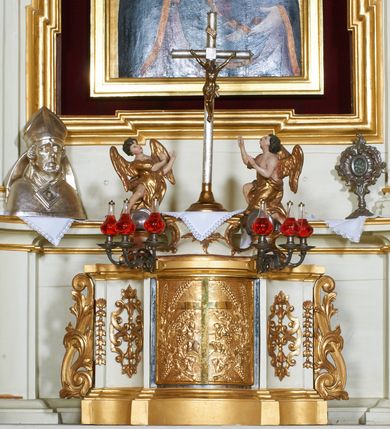 Zdjęcie nr 12: Ołtarz architektoniczny, drewniany, jednoosiowy, jednokondygnacyjny z bramkami. Mensa wąska, prostopadłościenna o ściankach wklęsło-wypukłych. Tabernakulum w kształcie prostopadłościennej skrzynki z przodu o linii wklęsło-wypukłej z uskokami. Ustawione jest na  wysokim cokole, flankowane parą szerokich, wklęsłych pilastrów, zdobionych ornamentem złożonym z przeplatających się wolut i kampanul. Ścianka frontowa wypukła, w polu prostokątne, metalowe drzwiczki, zdobione kiśćmi winogron i kłosami zbóż, pośrodku łaciński prosty krzyż. Całość zamknięta profilowanym gzymsem. Po bokach tabernakulum zwisy z kampanul, a na skrajach płaskorzeźbione uszy z liści akantu.  Do górnej krawędzi przybite gwoździem na trzech tulejach lampki oliwne. Nad tabernakulum tron wystawienia z rzeźbionymi w drewnie aniołkami na obłokach adorującymi krucyfiks. 

Retabulum ustawione na zdwojonym cokole, ujęte zwielokrotnionymi pilastrami toskańskimi i dwiema kolumnami kompozytowymi na wysokich cokołach, ustawionymi pod kątem i podtrzymującymi profilowane, przerwane belkowanie. Pilastry od strony wewnętrznej ołtarza są wklęsłe, ozdobione dwiema parami uskrzydlonych główek anielskich i zwisami z kwiatów; od zewnątrz pilastry mają trzony wypukłe.  W polu głównym wnęka, ujęta ramą w kształcie stojącego prostokąta o uszatych narożach. We wnęce na czerwonym tle umieszczony obraz Matki Boskiej Piekarskiej, na zasuwach obrazy „Koronacja Matki Boskiej” oraz „Św. Mikołaj”. Nad obrazem kartusz o kształcie zbliżonym do rombu z ornamentami rocaille'owymi wokół; w polu napis „ALTARE / PRIVILEGI/ATUM”. Na osi kolumn, na przyczółku ustawione są wazony z kwiatami. 

Zwieńczenie w kształcie stojącego prostokąta, flankowane parą pilastrów podtrzymujących przerwane belkowanie, zamknięte gzymsem w formie łuku odcinkowego. Na szczycie promienista gloria z otokiem chmur pośrodku z płaskorzeźbionym monogramem IHS. W polu głównym obraz przedstawiający Ekstazę św. Teresy w kształcie stojącego prostokąta, zamknięty łukiem nadwieszonym. Po bokach zwieńczenia uszy z liści akantu i kwiatów. Pod obrazem uskrzydlona para główek aniołków. 

Bramki w formie stojącego prostokąta, flankowane węgarami, zamknięte wolutowym łukiem z ustawionymi na szczycie na niskich cokołach rzeźbami świętych: po lewej św. Piotra, a po prawej św. Pawła.  Przejście zamknięte łukiem wklęsło-wypukłym z uskokami. Struktura polichromowana w kolorze jasnobeżowym, ornamentyka złocona, detale srebrzone.
